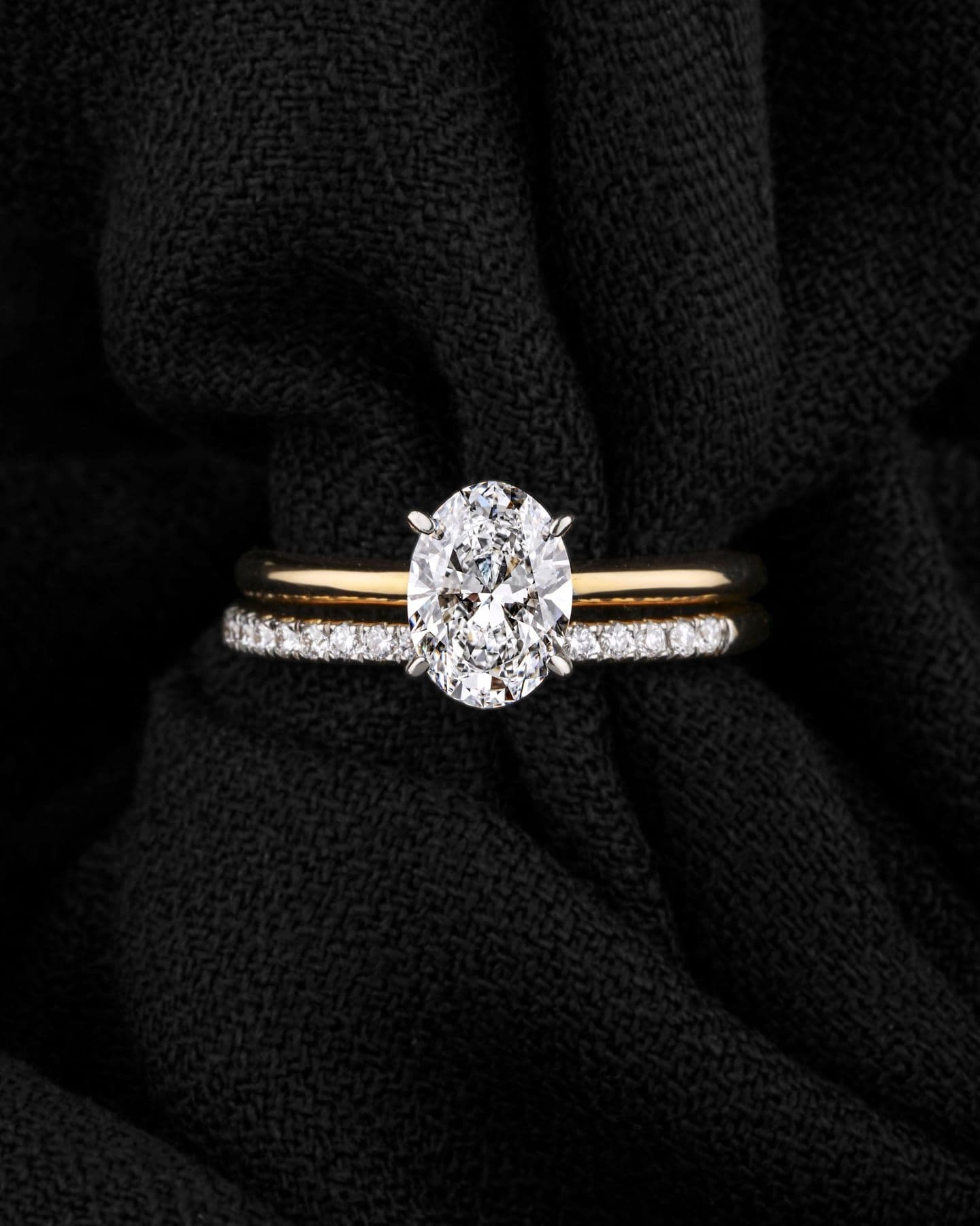 Oval diamond engagement ring resting on black textured fabric
