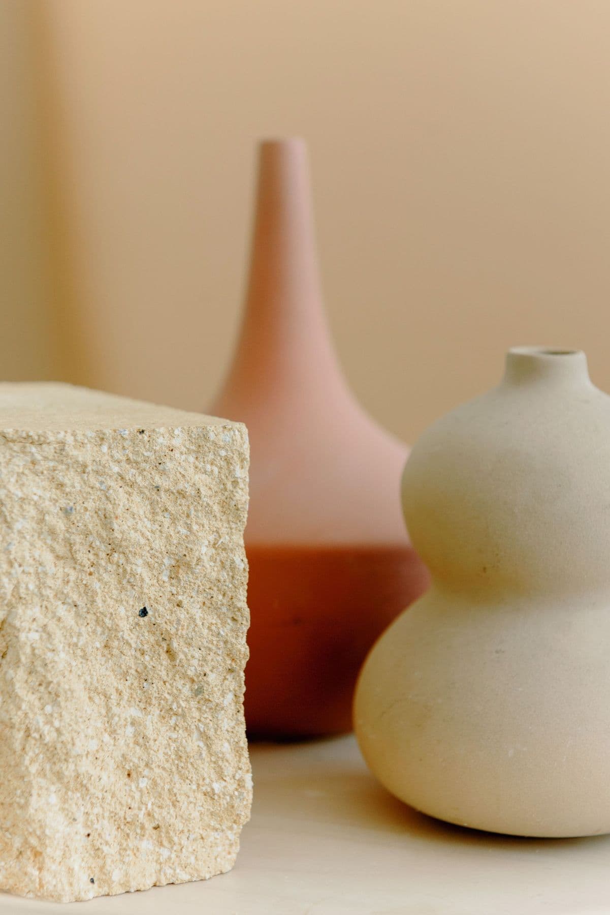 Sculptural ceramic vases beside a textured stone cube in soft light