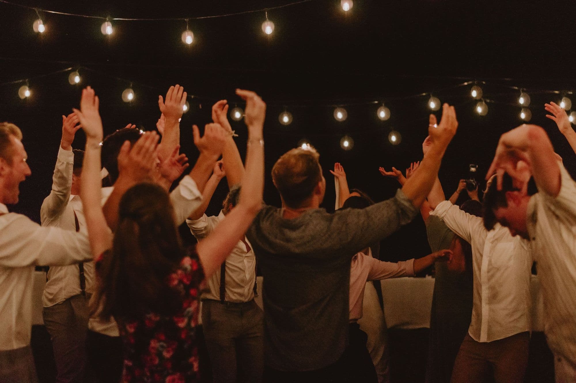 Guests dancing with arms raised beneath string lights at an evening party
