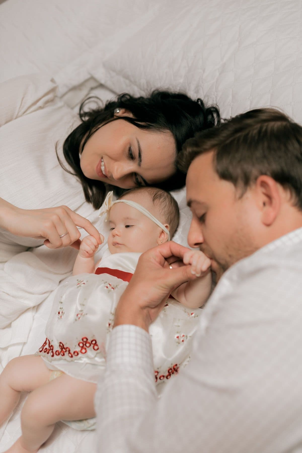 New parents lying beside their newborn daughter on a white bed