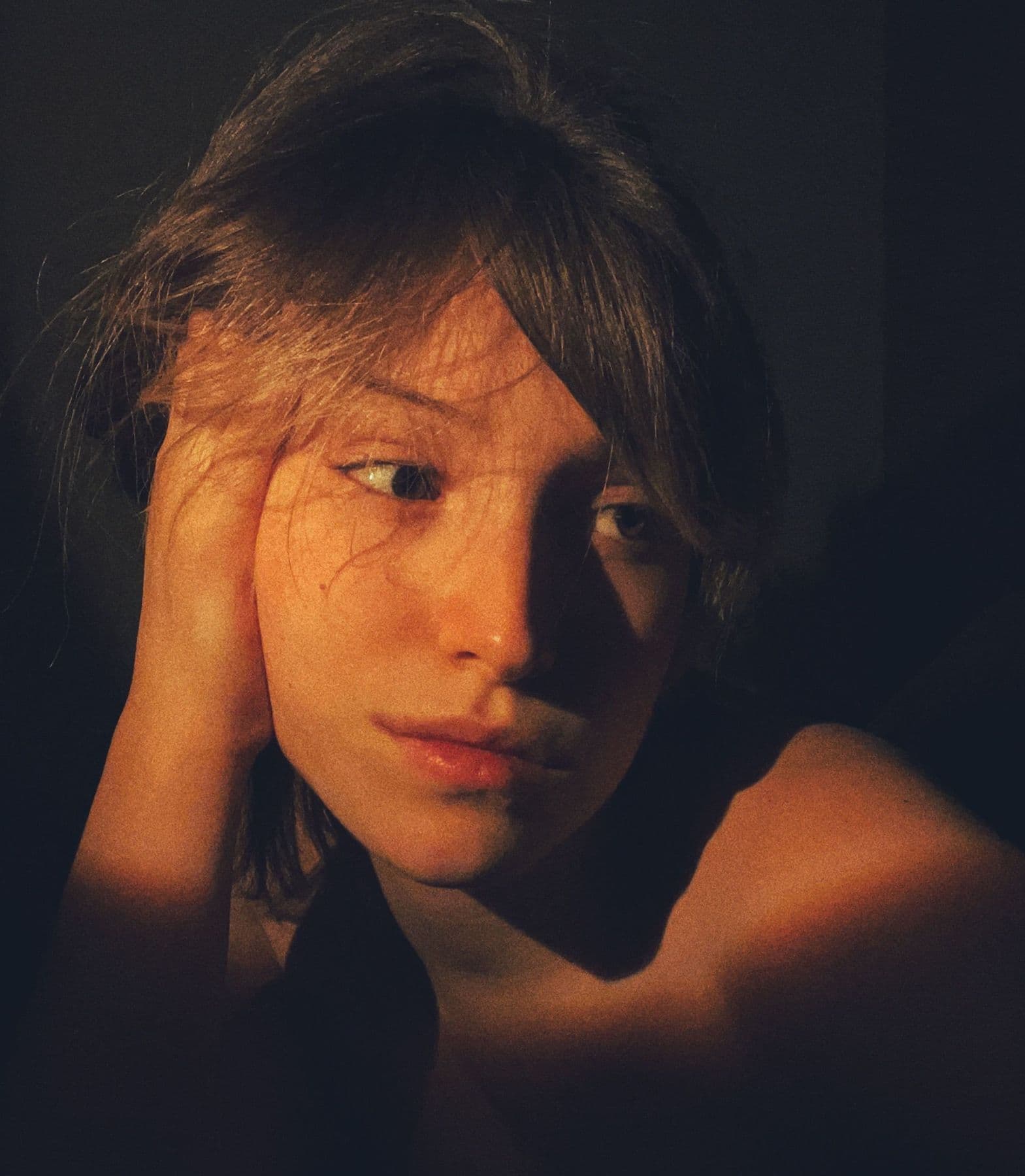 Young woman resting her head on her hand, face lit by warm side light