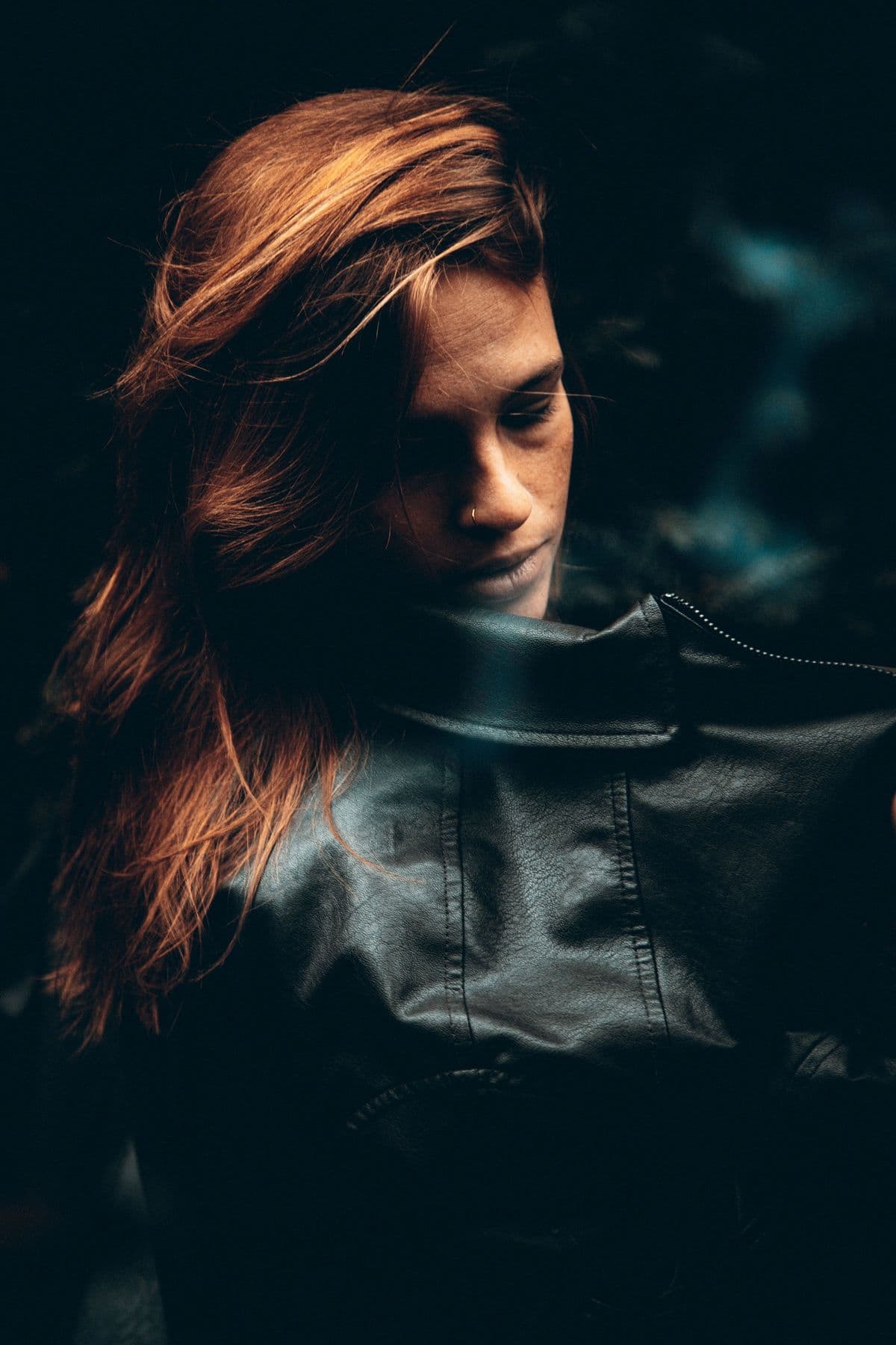 Red-haired woman in a leather jacket photographed in dark, moody tones