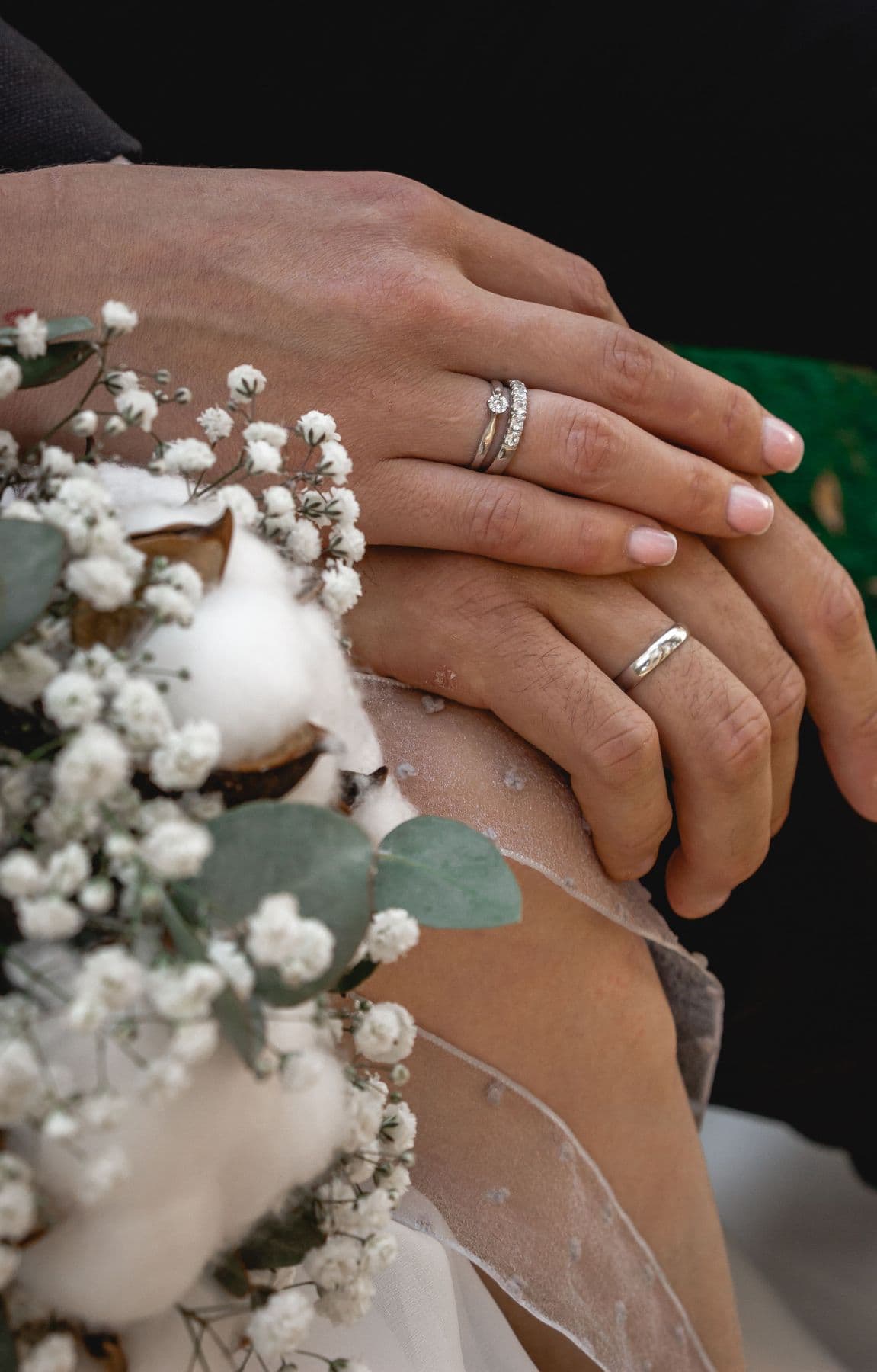 Close-up of a couple's hands wearing wedding bands above a bouquet of baby's breath