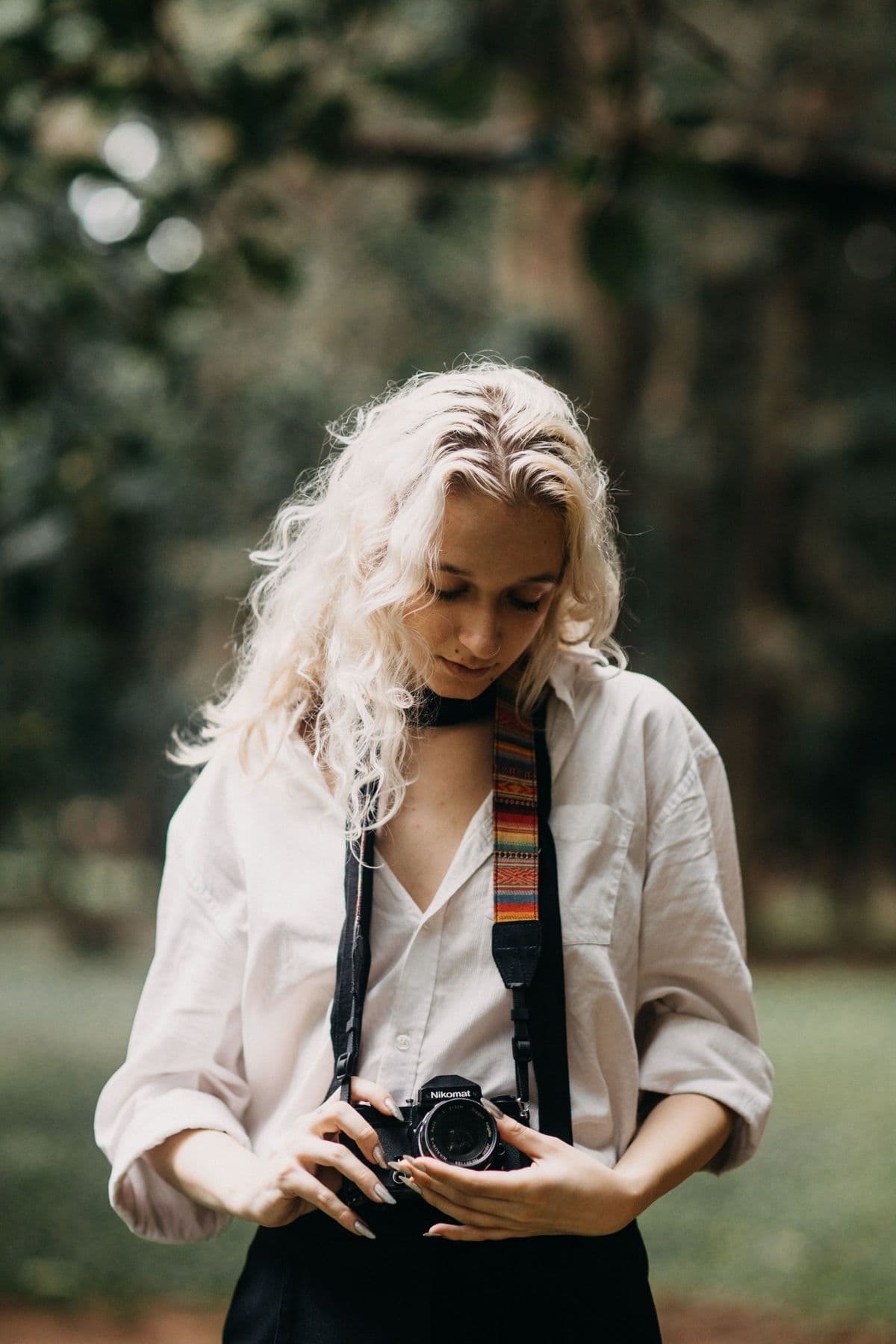 Portrait of photographer Amara Cole holding a film camera outdoors among the trees