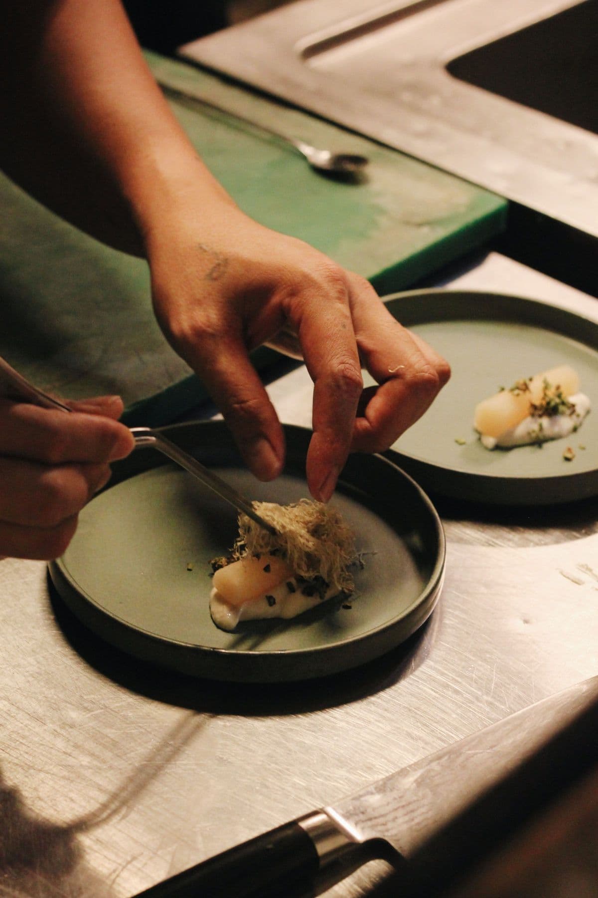 Chef's hands plating a delicate course on a dark ceramic dish
