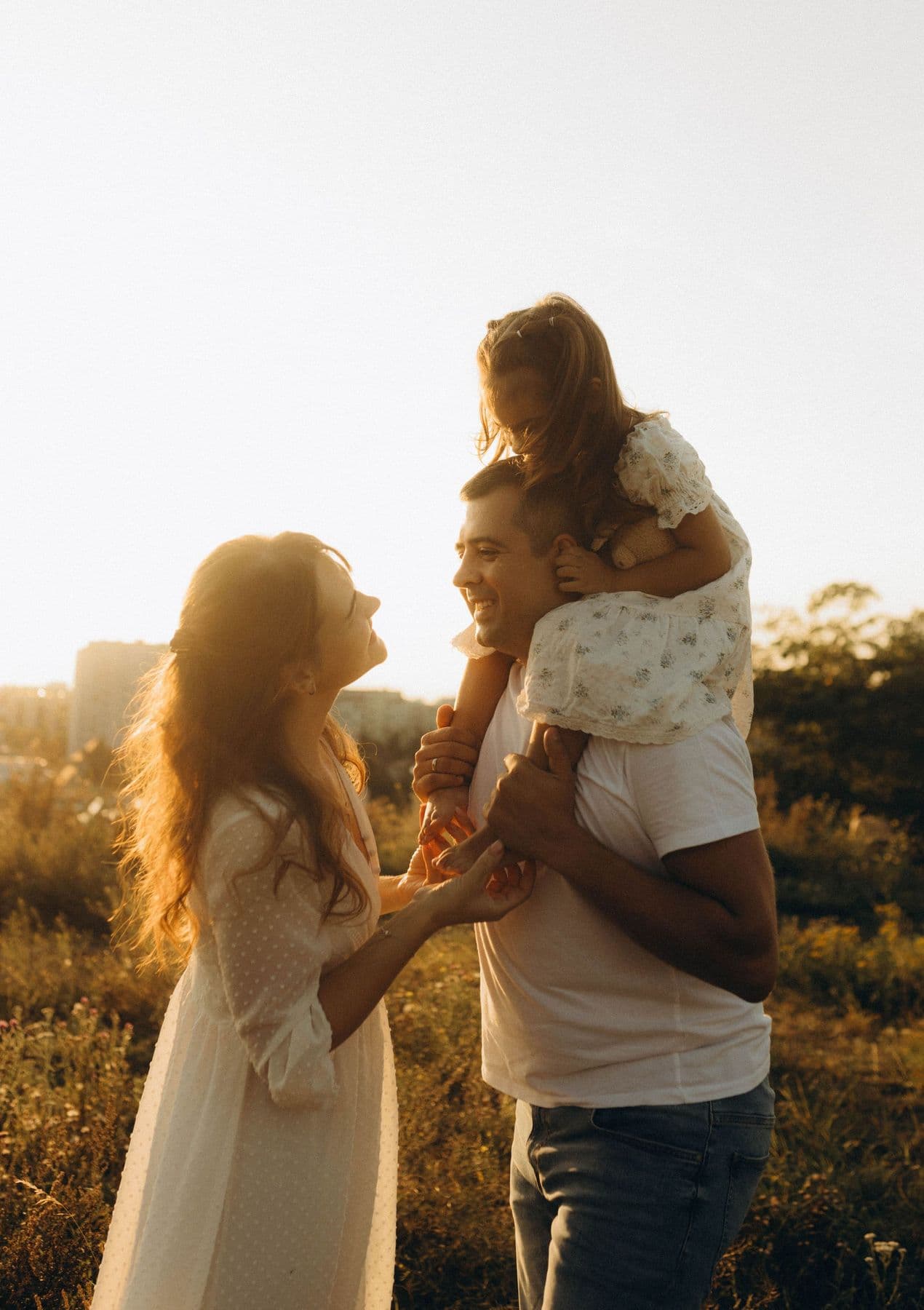 Father carrying his daughter on his shoulders beside her mother in golden evening light