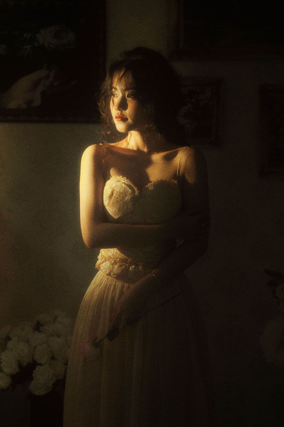 Woman in a vintage lace dress standing in warm lamplight in a dim room