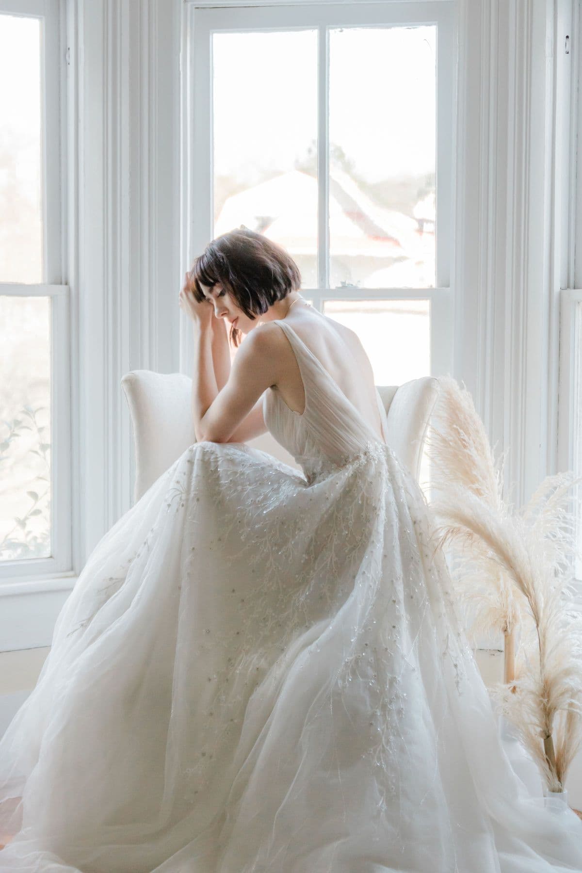 Bride in a voluminous gown seated by a window, head bowed in a quiet moment